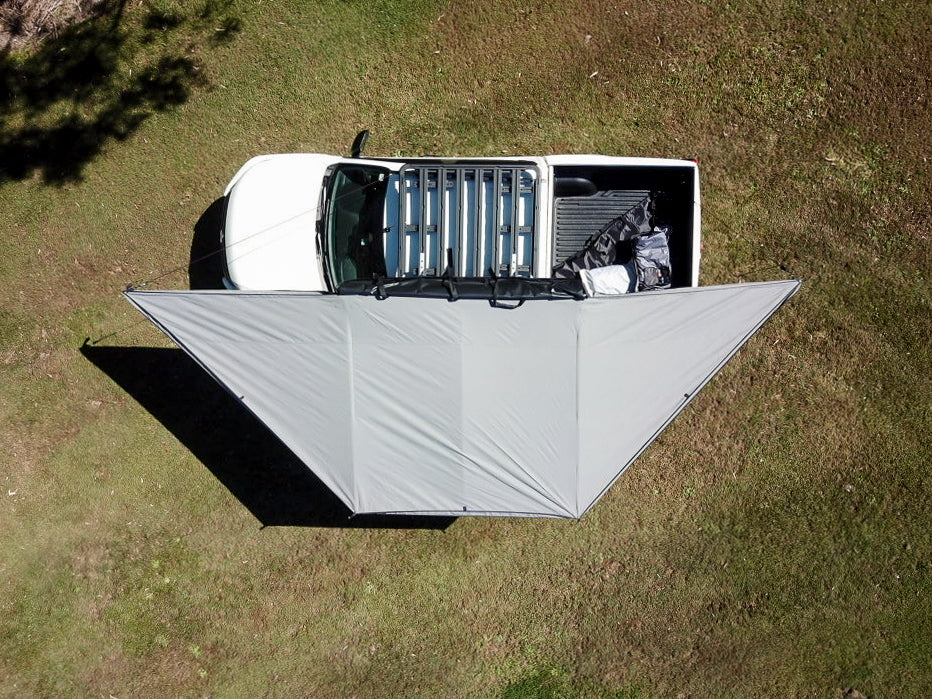 Top-down photo of an open OUTBOUND Shield 3 Freestanding Awning mounted on a white dual cab Ute. Set on grass with trees in the background.